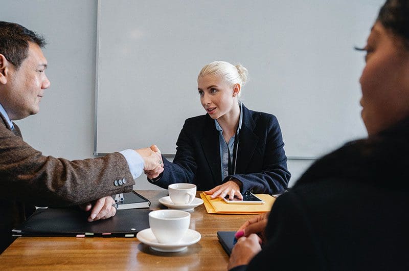 Two business people shaking hands at a meeting table.